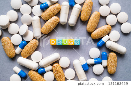 An arrangement of pills, capsules, and supplements with colorful blocks in the middle spelling out the word DRUGS 121168439