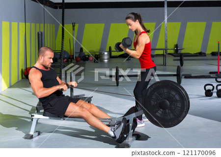 Gym couple with dumbbell weights and fitness rower Gym couple with dumbbell weights and fitness rower 121170096