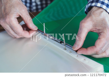 Elderly female hands with green plastic file folder, person fix files with a metal clip, close-up, selective focus. 121170472