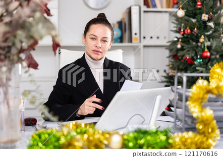 Portrait of successful business woman with New Years tinsel and Christmas tree in office 121170616