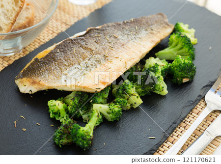 Fried fillet of sea bass with garnish of broccoli on black warm stone plate Fried fillet of sea bass with garnish of broccoli on black warm stone plate 121170621