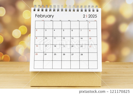 February 2025 desk calendar on wooden table with gold light bokeh. 121170825