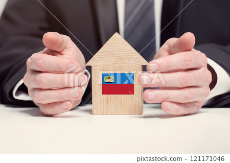 Businessman hand holding wooden home model with Liechtenstein flag. insurance and property concepts Businessman hand holding wooden home model with Liechtenstein flag. insurance and property concepts 121171046