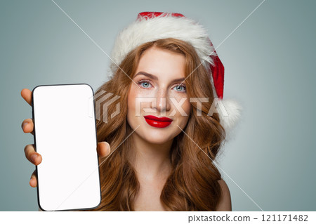 Pretty young smiling woman in red Santa hat showing smartphone Pretty young smiling woman in red Santa hat showing smartphone 121171482
