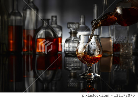 Brandy is poured from a bottle into a glass. Brandy is poured from a bottle into a glass. 121172070