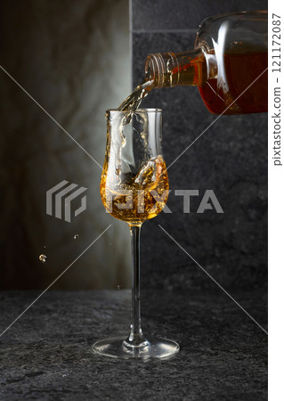 Pouring strong alcoholic drink from a bottle into a glass. 121172087
