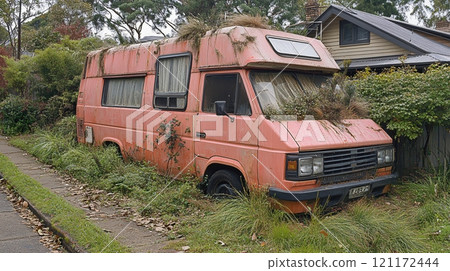 Old campervan forgotten on a street surrounded by overgrown grass and weeds 121172444