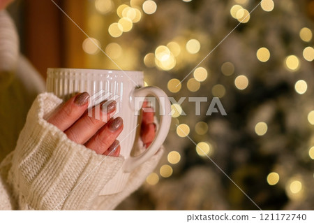 Hands, Mug, Christmas - Woman holds warm beverage in front of blurred Christmas lights. Hands, Mug, Christmas - Woman holds warm beverage in front of blurred Christmas lights. 121172740