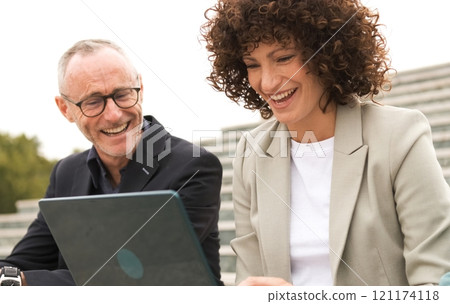 Cheerful business colleagues using netbook sitting on steps Cheerful business colleagues using netbook sitting on steps 121174118