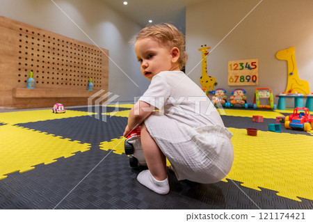 Toddler playing with a toy in a colorful playroom. Concept of child development and fun exploration Toddler playing with a toy in a colorful playroom. Concept of child development and fun exploration 121174421