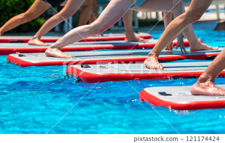 Feet balancing on paddleboards during yoga in a resort pool. Concept of outdoor fitness and tropical recreation 121174424