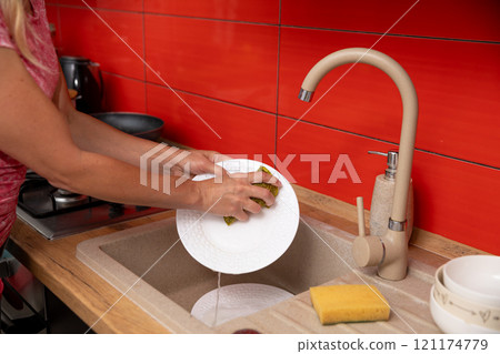 A person washes dishes in a colorful kitchen, emphasizing cleanliness and personal responsibility 121174779
