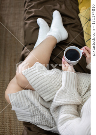 Embrace a cozy lifestyle while enjoying coffee in a comfortable sweater on the sofa 121174810