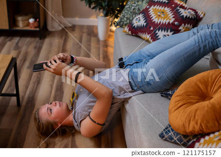 A Relaxed Teenager is Sitting Comfortably on a Cozy Couch While Enjoying a Mobile Game A Relaxed Teenager is Sitting Comfortably on a Cozy Couch While Enjoying a Mobile Game 121175157