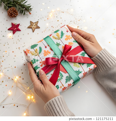 Human hands holding wrapped Christmas gift box with red ribbon 121175211