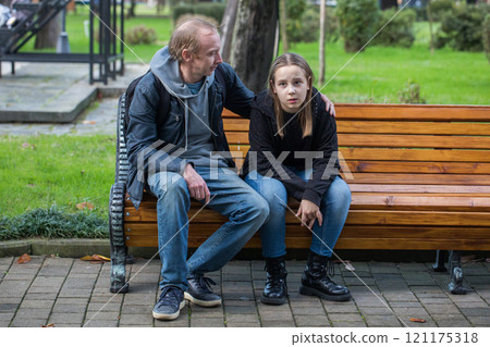Tired child girl with father sitting on the bench, outdoor portrait 121175318