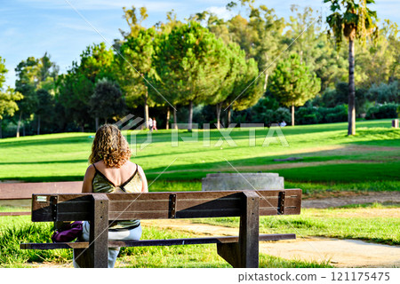 Blonde curly haired woman sitting on a bench in La Retama park in Alcala de Guadaira, Seville, Spain Blonde curly haired woman sitting on a bench in La Retama park in Alcala de Guadaira, Seville, Spain 121175475