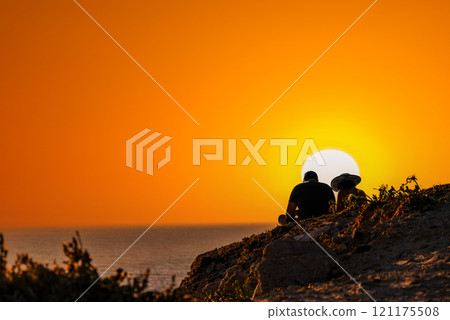 Young couple watching the sunset on Barbate beach next to the Trafalgar lighthouse, Cadiz Young couple watching the sunset on Barbate beach next to the Trafalgar lighthouse, Cadiz 121175508