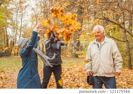 Happy grandfather, muther and little child girl having fun with yellow autumn leaves on nature background outdoor 121175569