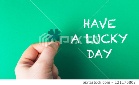A hand holding a shamrock and the words have a lucky day written below it A hand holding a shamrock and the words have a lucky day written below it 121176802