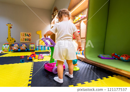 Young child playing on a bright playmat in a toy-filled playroom. Concept of exploration and joyful learning Young child playing on a bright playmat in a toy-filled playroom. Concept of exploration and joyful learning 121177537