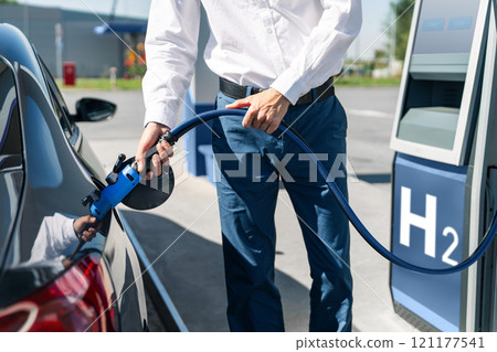 Man holds a hydrogen fueling nozzle on a hydrogen filling station. Refueling car with hydrogen fuel Man holds a hydrogen fueling nozzle on a hydrogen filling station. Refueling car with hydrogen fuel 121177541