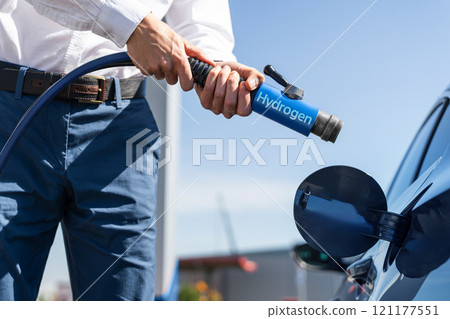 Man holds a hydrogen fueling nozzle on a hydrogen filling station. Refueling car with hydrogen fuel Man holds a hydrogen fueling nozzle on a hydrogen filling station. Refueling car with hydrogen fuel 121177551