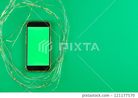 On a bright green background lies a phone with a green chroma key screen surrounded by a garland that glows yellow with space for text. High quality photo On a bright green background lies a phone with a green chroma key screen surrounded by a garland that glows yellow with space for text. High quality photo 121177570
