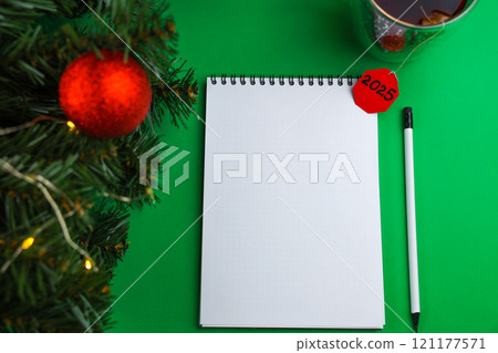 A white banknote and a white pencil with a black lead and a black eraser lie on a green background, next to it is a mug of black tea with a paper red label wishing a Happy New Year, on the left there A white banknote and a white pencil with a black lead and a black eraser lie on a green background, next to it is a mug of black tea with a paper red label wishing a Happy New Year, on the left there 121177571