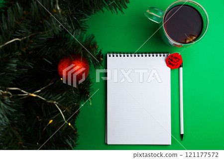 A white banknote and a white pencil with a black lead and a black eraser lie on a green background, next to it is a mug of black tea with a paper red label wishing a Happy New Year, on the left there A white banknote and a white pencil with a black lead and a black eraser lie on a green background, next to it is a mug of black tea with a paper red label wishing a Happy New Year, on the left there 121177572