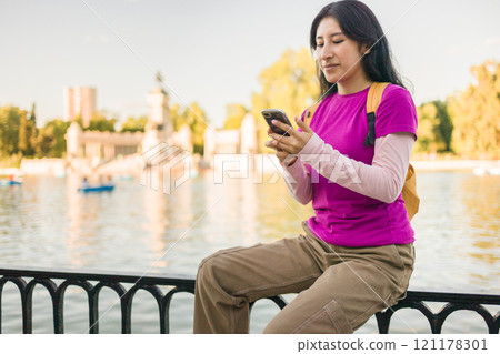 Young peruvian woman using smartphone in madrid's retiro park near the lake 121178301