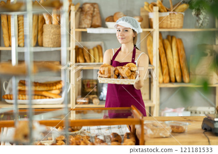 Bakery young woman employee holds basket of ready-made croissant 121181533