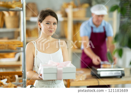 Cute young girl customer holding box with decorative bow and buying sweet authors flour products in bakery shop 121181689