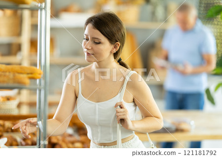 Interested girl looking at baked goods on shelves in display case in bakery store Interested girl looking at baked goods on shelves in display case in bakery store 121181792
