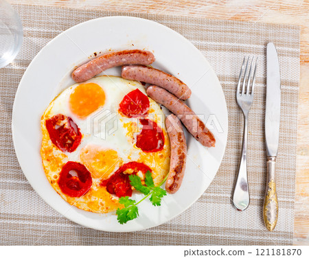 Homemade hearty breakfast - fried eggs with frankfurter and tomato 121181870