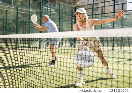 Motivated senior woman playing padel with her teammate in court Motivated senior woman playing padel with her teammate in court 121181901