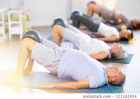 Group of mature women and men practicing pilates with soft ball in fitness studio 121181914