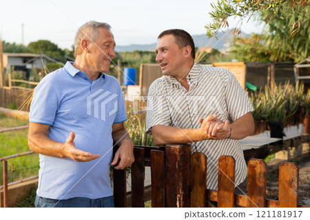 Two male gardeners talking near wooden fence in garden 121181917
