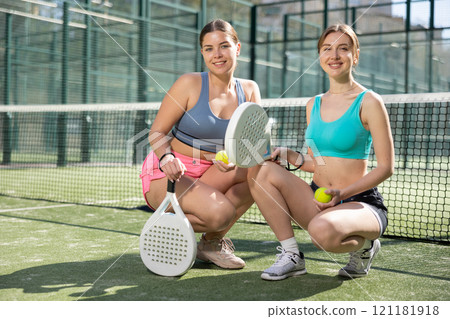 Two young sporty girls getting ready for padel game in court on sunny day 121181918
