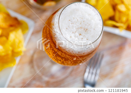 Glass of chilled frothy beer with snacks - potato chips and pickled olives. Glass of chilled frothy beer with snacks - potato chips and pickled olives. 121181945