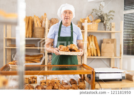 Bakery senior man employee holds basket of ready-made croissant Bakery senior man employee holds basket of ready-made croissant 121181950