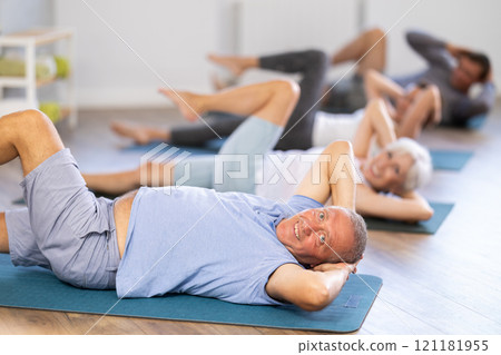 Elderly man performs exercises to strengthen abdominal muscles during group workout 121181955