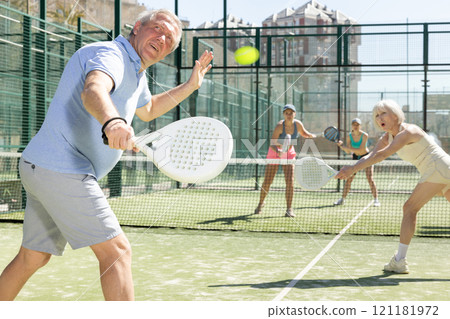 Determined sporty older man doing his best playing padel in court 121181972