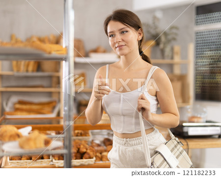 Interested girl looking at baked goods on shelves in display case in bakery store 121182233