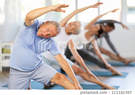 Mature male participant working out practice Parighasana, bolt pose with students group 121182307