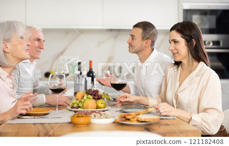 Mature married couple are sitting at table, enjoying food and wine with middle-aged guests. Mature married couple are sitting at table, enjoying food and wine with middle-aged guests. 121182408