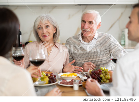 Mature married couple are sitting at table, enjoying food and wine with middle-aged guests. 121182490