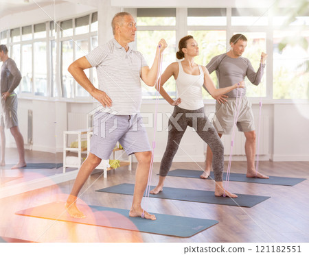 Mature man stretches his body using an expander in group Pilates training 121182551