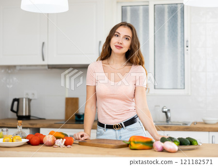Smiling woman chopping vegetables in home kitchen, preparing vegan dish 121182571