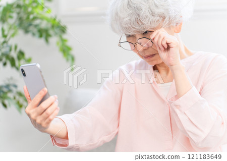 一位患有老花眼且看不清智慧型手機的老年女性 121183649